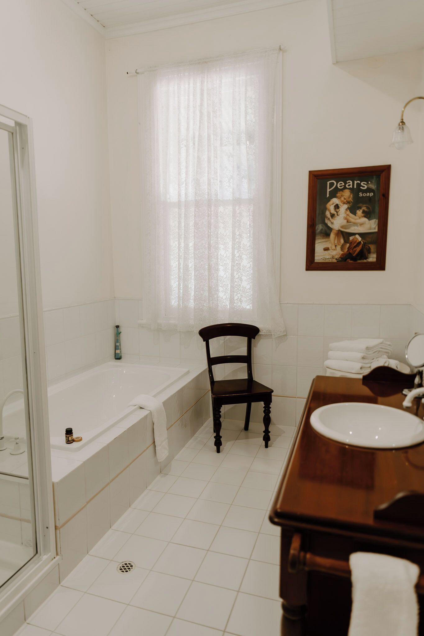 Une salle de bain avec une baignoire, une chaise en bois, un lavabo et une fenêtre avec un rideau.