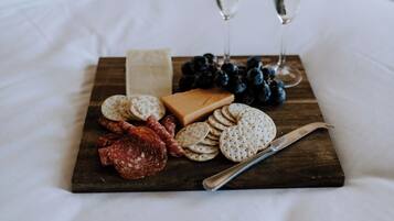 Ein Holzbbrett mit Snacks und zwei Gläsern Weißwein auf einem Bett.