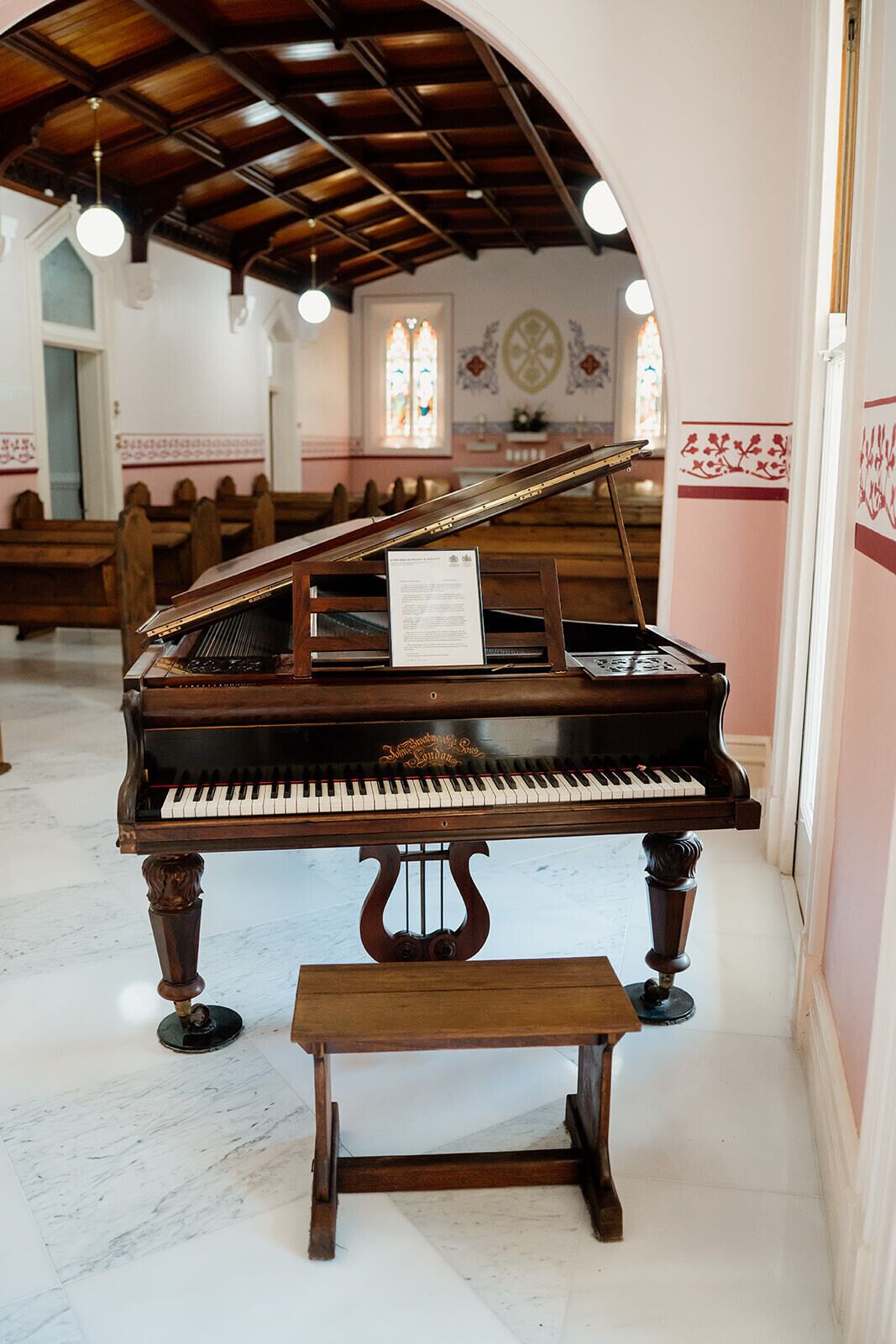 A grand piano in a church with pews, a wooden bench, and stained glass windows.