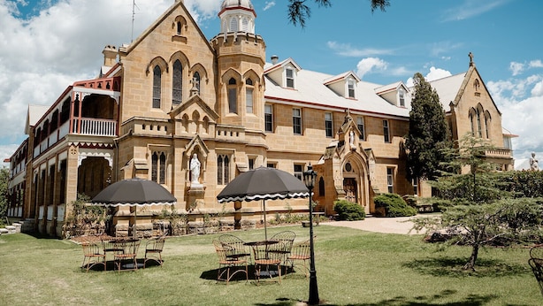 A large, historic building with a prominent tower and arched windows, surrounded by a well-maintained lawn and outdoor seating area. - The Abbey (Warwick)