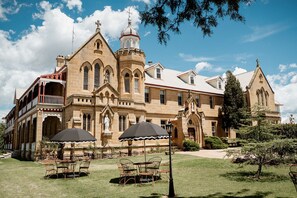A large, historic building with a prominent tower and arched windows, surrounded by a well-maintained lawn and outdoor seating area. - The Abbey (Warwick)