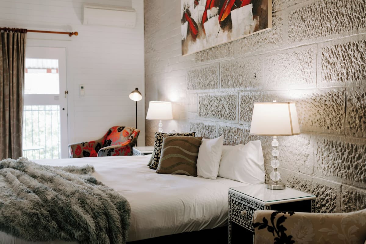 Un dormitorio ordenado con una cama grande, dos lámparas de noche, una manta estampada y una silla con tapicería floral.