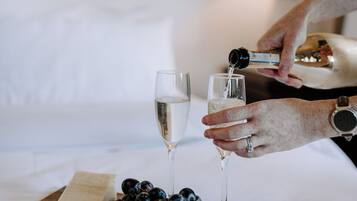 A person pouring champagne into a glass on a wooden board with cheese, crackers, and grapes.