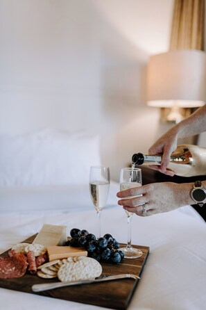 A person pouring champagne into a glass on a wooden board with cheese, crackers, and grapes.
