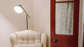 A room with a cream-colored armchair, a floor lamp, and a red door with a frosted glass panel.