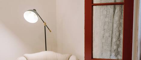 A room with a cream-colored armchair, a floor lamp, and a red door with a frosted glass panel.