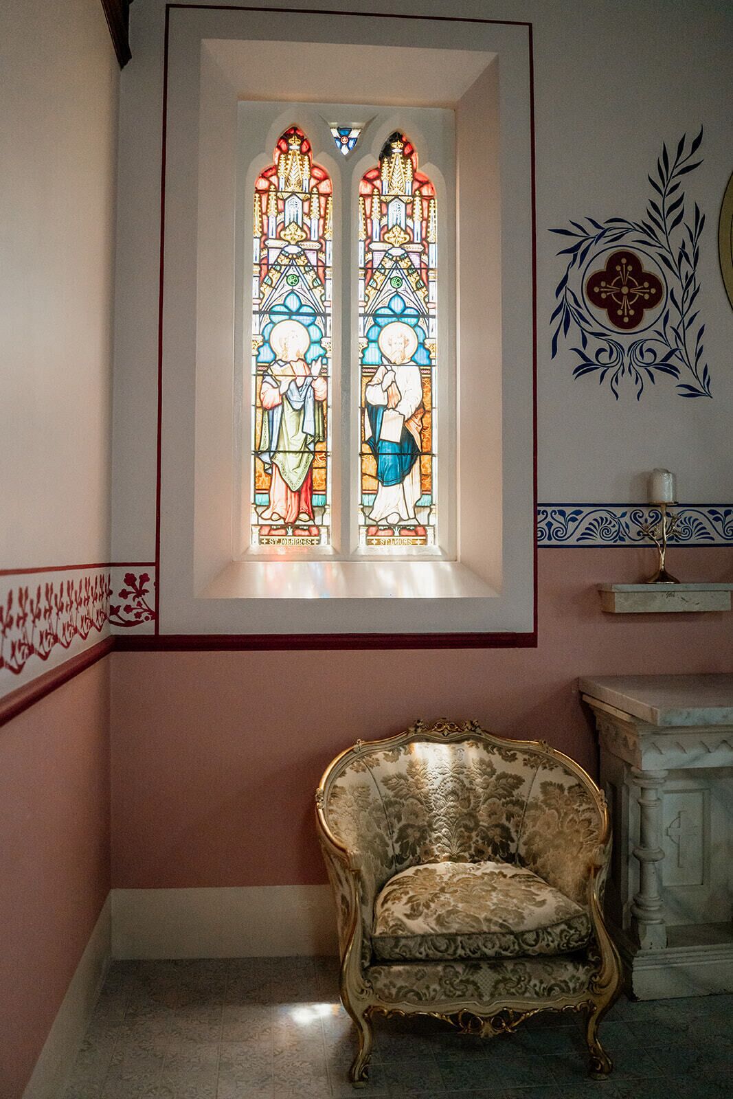 A room with a large stained glass window, a decorative chair, and a fireplace.