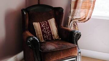 A corner room with a dark brown leather armchair, a white lamp, and a patterned curtain.