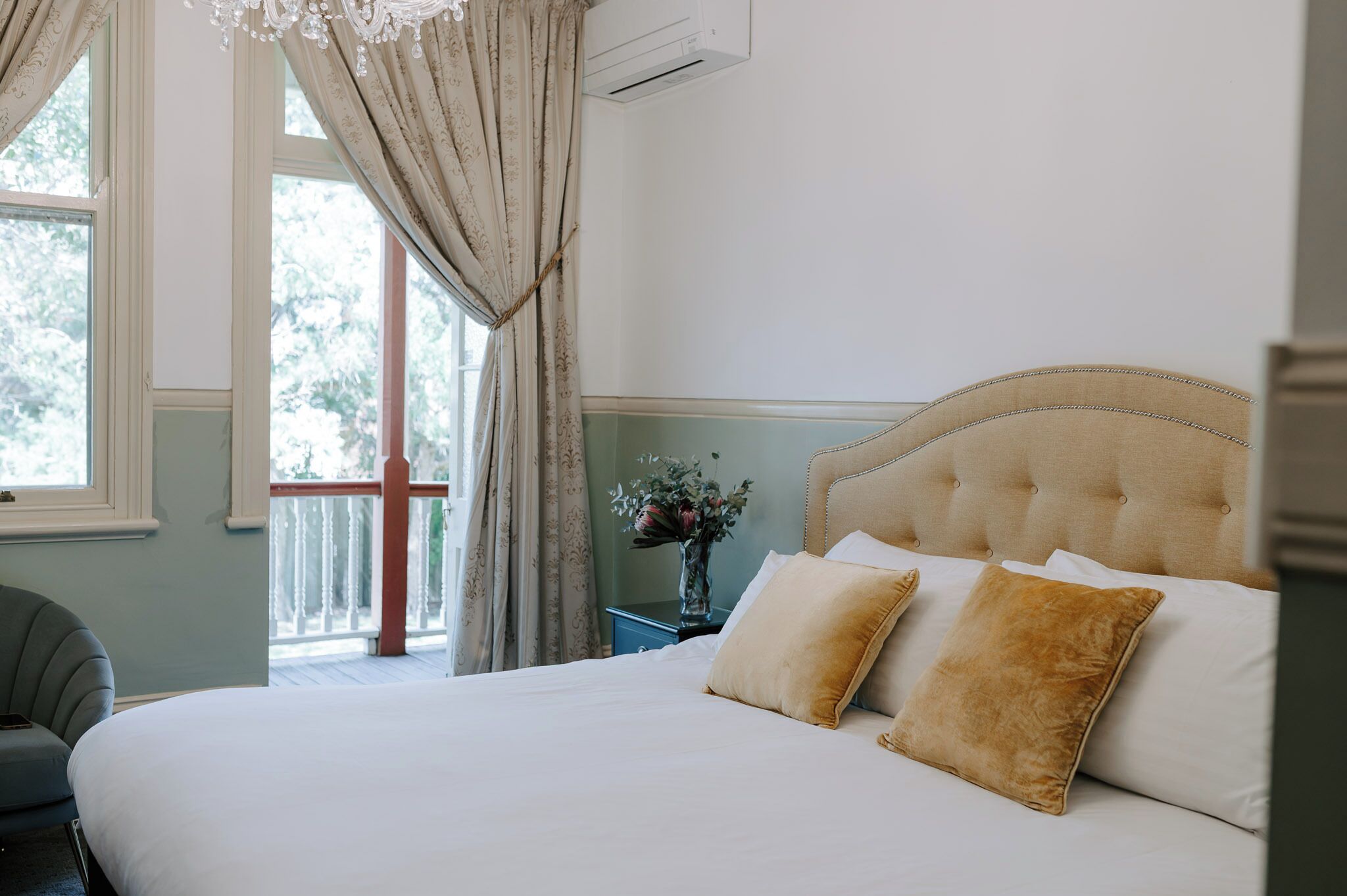 A bedroom with a large bed, a nightstand with a vase of flowers, and a window with curtains.