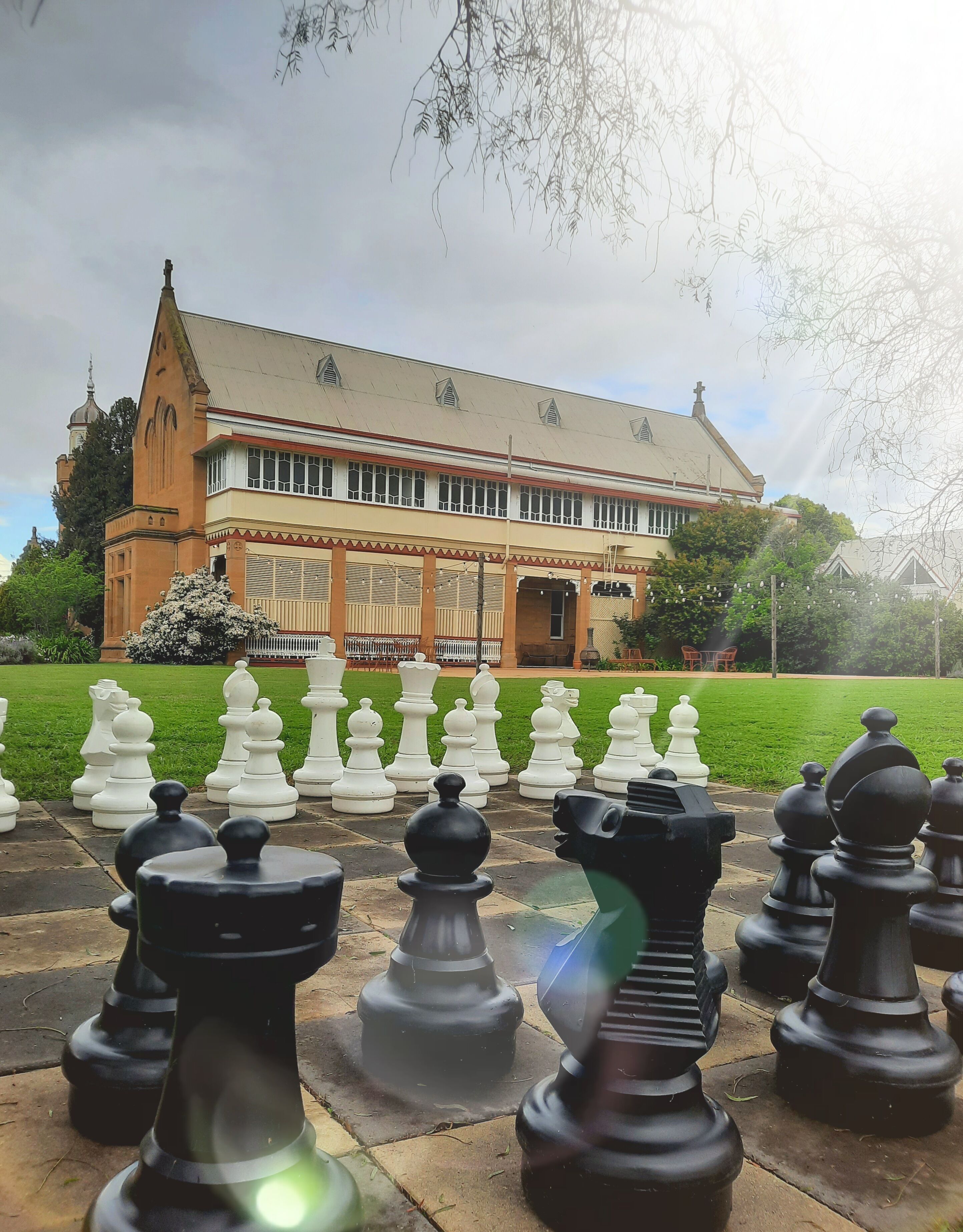 A chessboard set up in a garden with a building in the background.