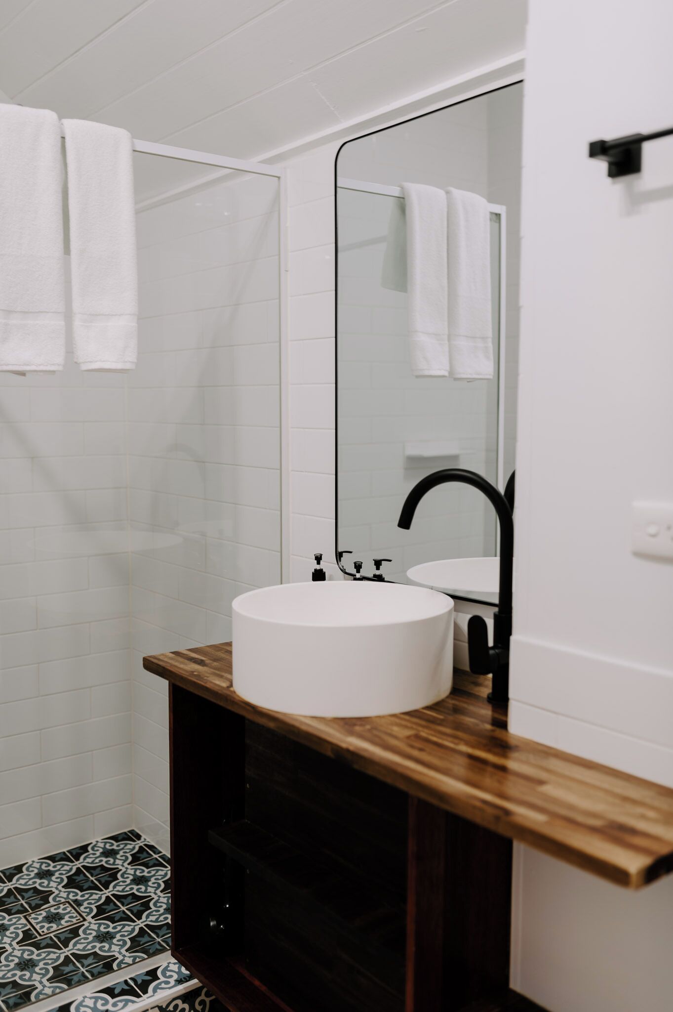 A modern bathroom with a white sink, wooden vanity, and a glass shower enclosure.