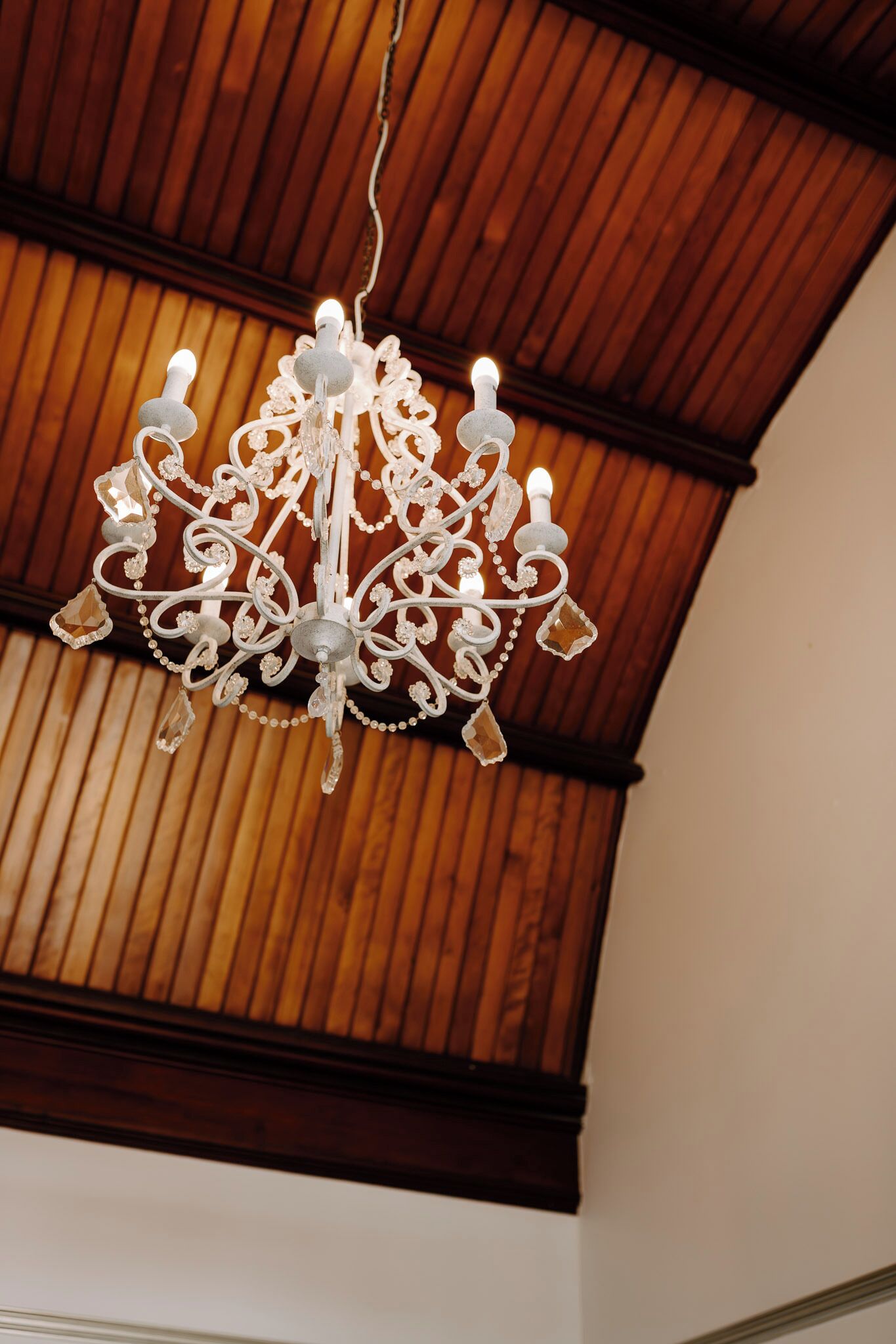 Un candelabro con intrincados detalles de metal y detalles de cristal, colgando de un techo de madera con diseño inclinado.