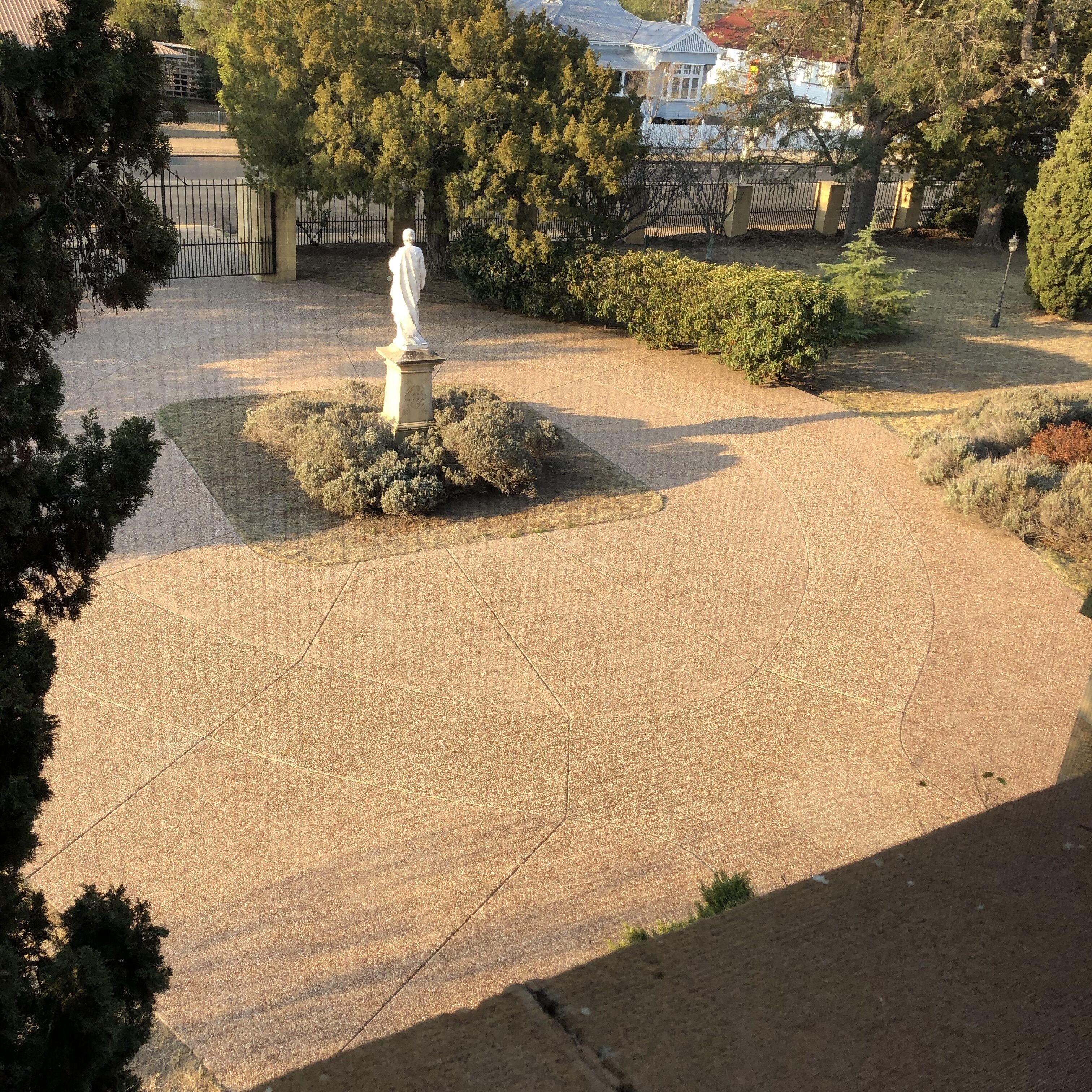 Un patio empedrado con una estatua en el centro, rodeado de árboles y arbustos.
