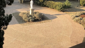 Un patio empedrado con una estatua en el centro, rodeado de árboles y arbustos.
