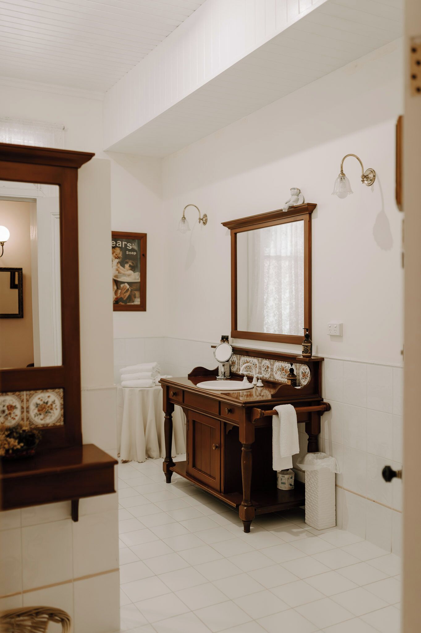 A bathroom with a wooden vanity, a large mirror, and a wall-mounted light fixture.