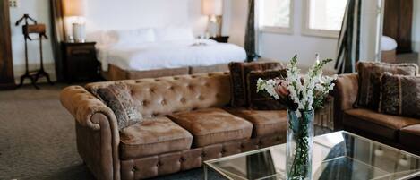 A bedroom with a large bed, a brown sofa, a glass coffee table, and a vase with flowers.