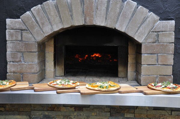 A brick oven pizza oven with four pizzas on wooden cutting boards in front.