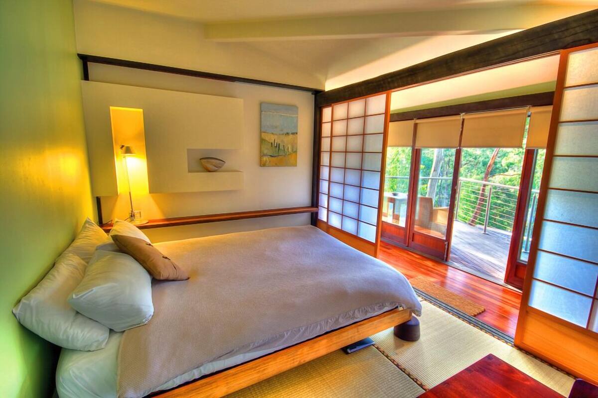 A traditional Japanese-style bedroom with tatami flooring, a low wooden bed, and sliding shoji doors leading to a balcony.