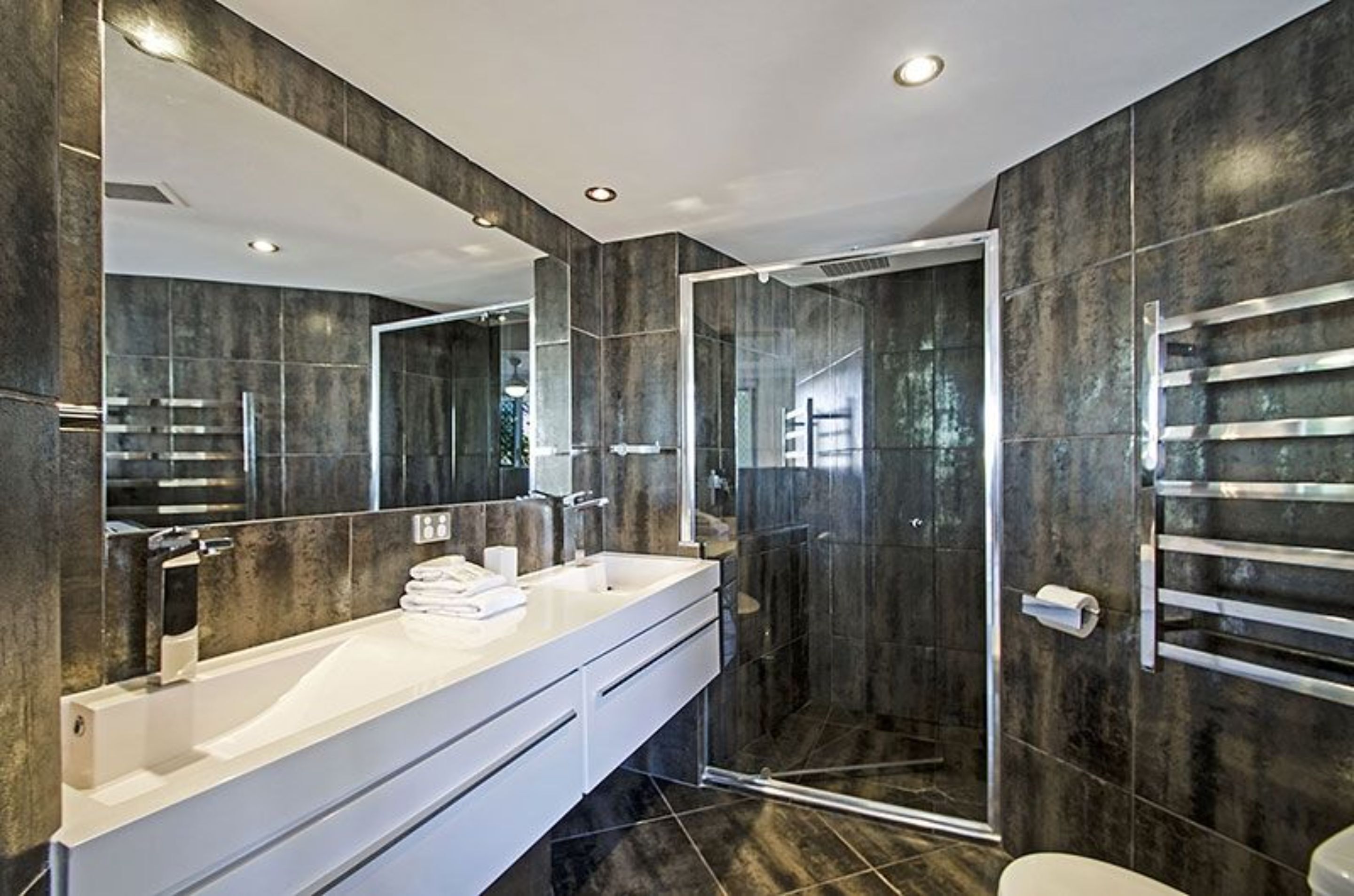 Un baño moderno con un espejo grande, tocador blanco y ducha con cerramiento de vidrio.