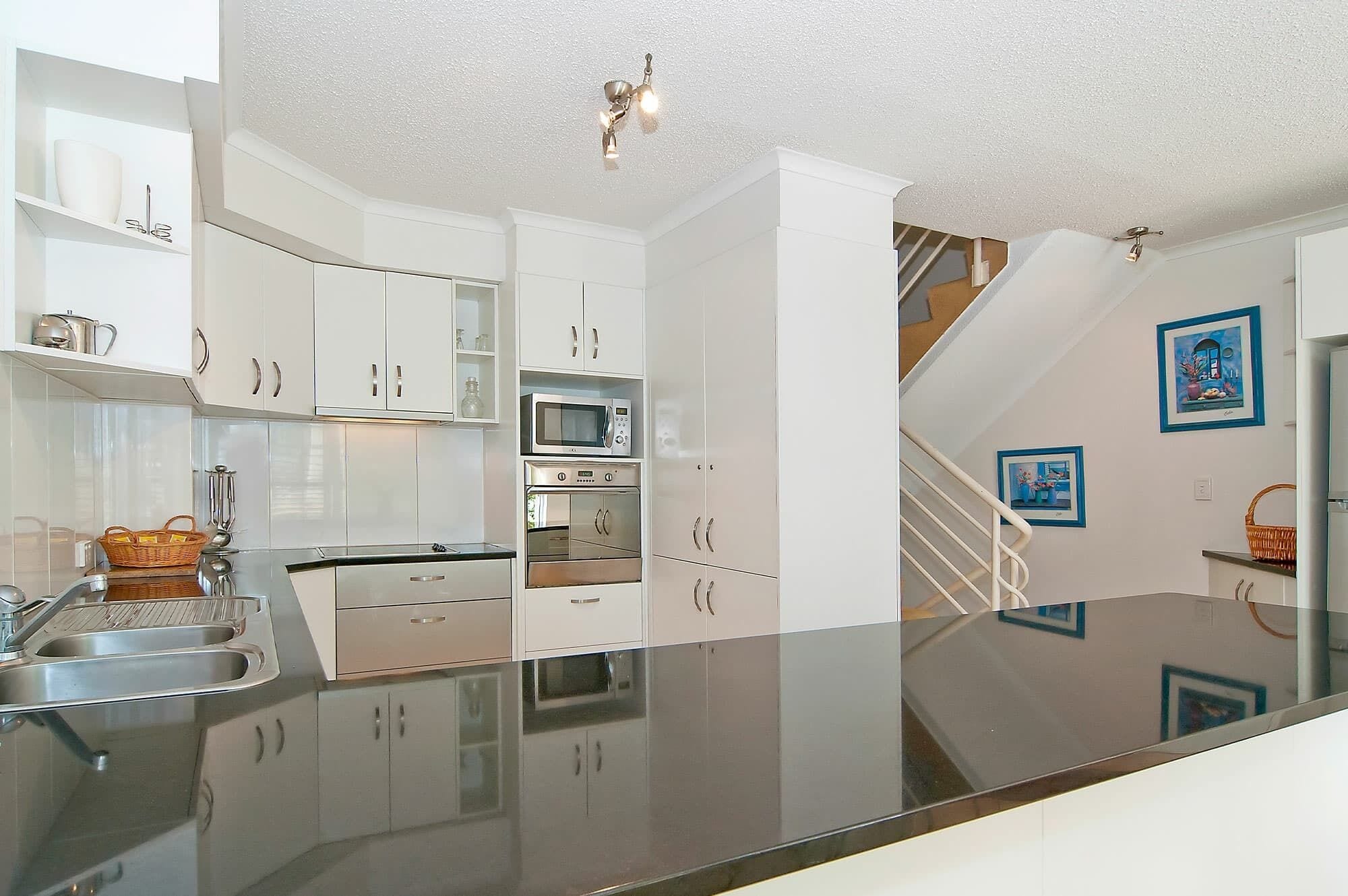 A modern kitchen with white cabinets, stainless steel appliances, and a reflective countertop.