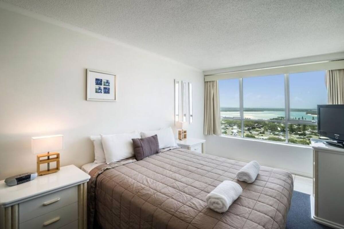 Een hotelkamer met een groot bed, een televisie, een bureau en een raam met uitzicht op het strand.