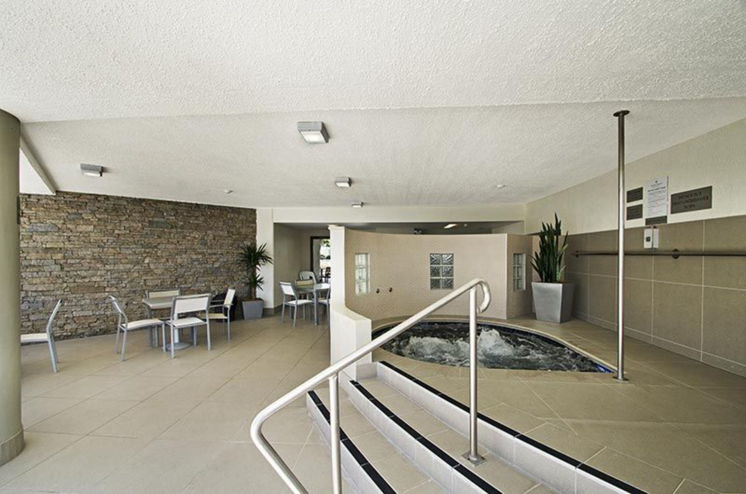 A spacious indoor area with a stone wall, a seating area with chairs, a small pool, and a staircase leading to an upper level.