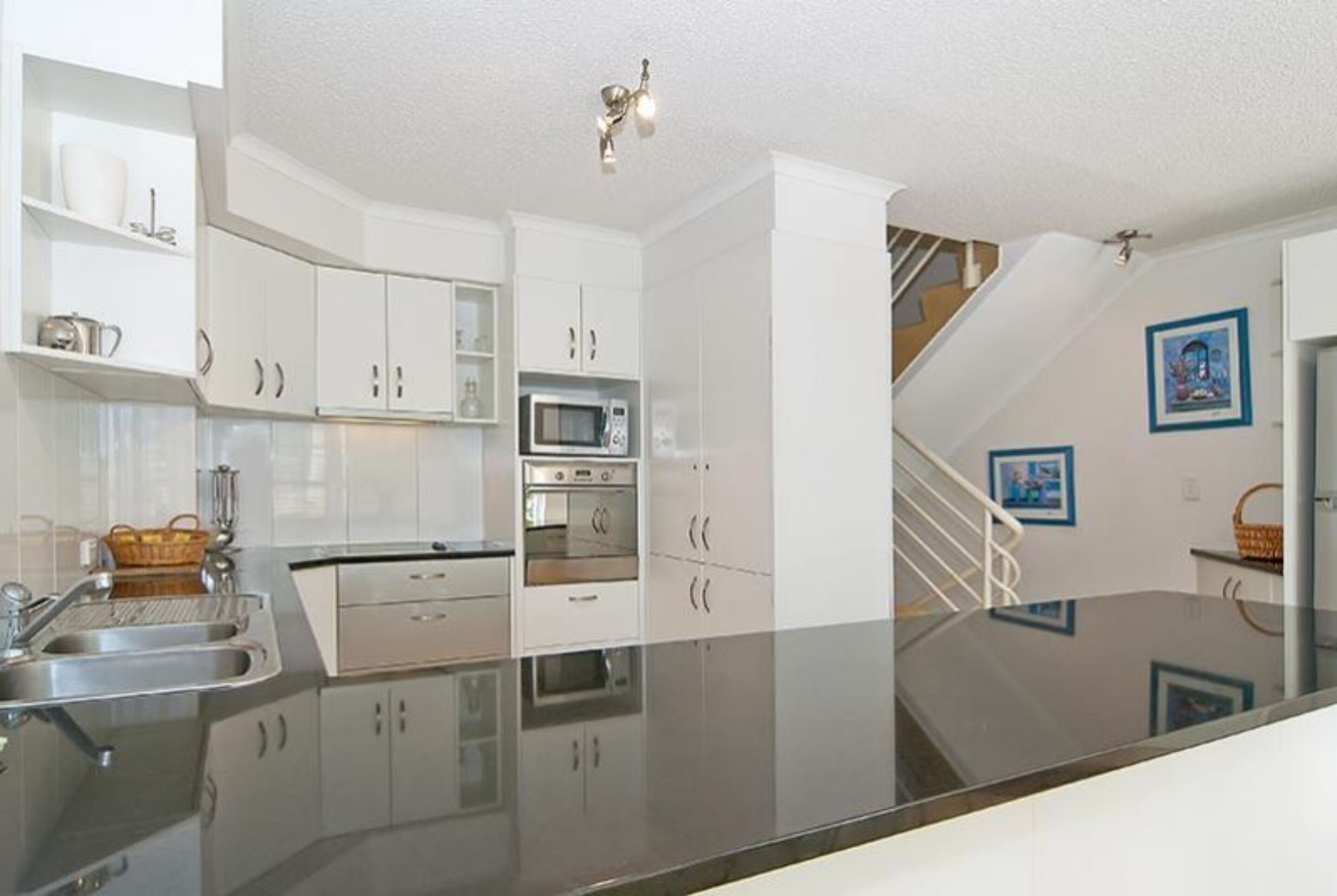 A modern kitchen with white cabinets, stainless steel appliances, and a glass countertop.