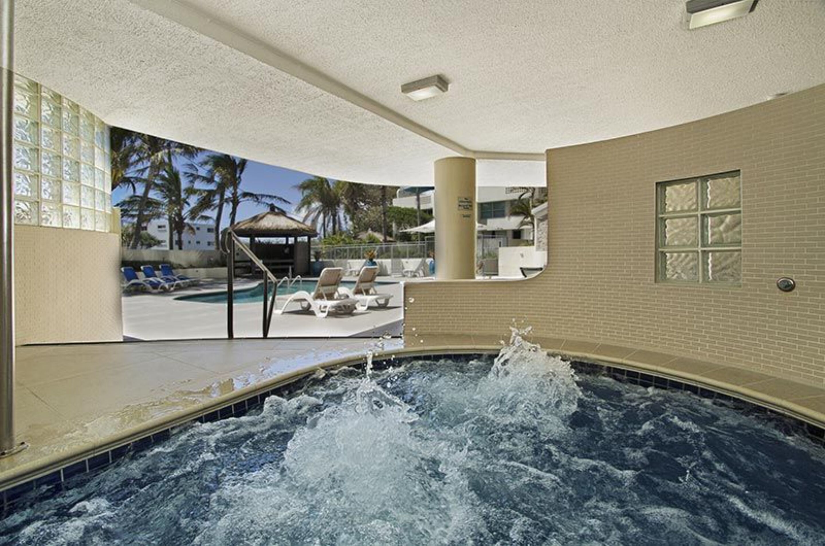 A hot tub area with a view of a pool and palm trees.