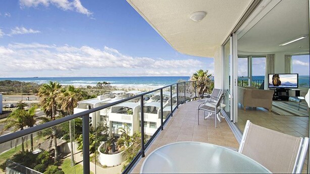 Een balkon met uitzicht op het strand en de oceaan, een zwembadgedeelte met ligbedden, en een televisie.