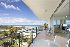 A balcony with a view of the beach and ocean, a pool area with lounge chairs, and a television. - Chateau Royale Beach Resort Maroochydore  (Maroochydore)