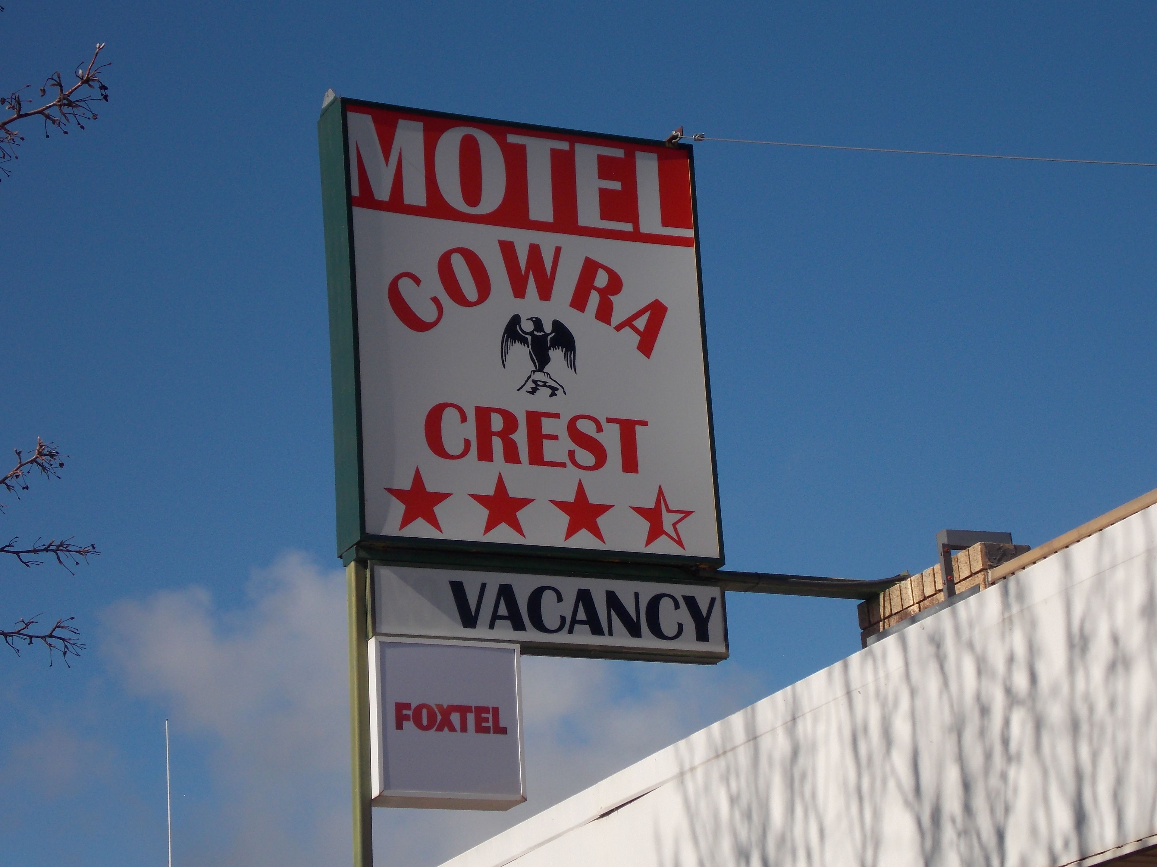 A motel sign with 'MOTEL COWRA CREST VACANCY' and 'FOXTEL' branding.