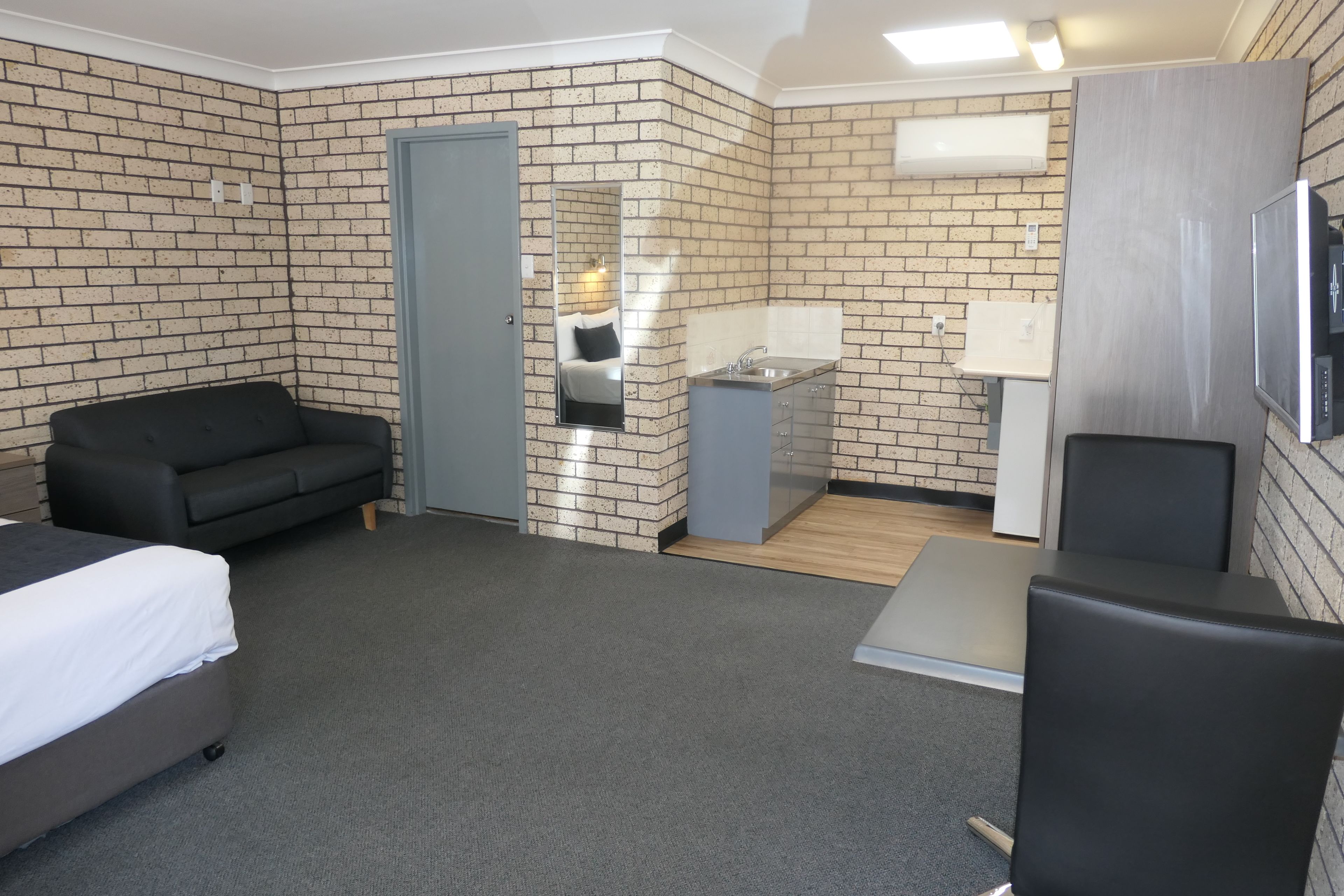 Une chambre d’hôtel avec un mur en briques, un lit, un canapé, un bureau et une salle de bain équipée d’un miroir et d’un lavabo.