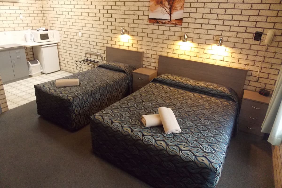 A hotel room with two beds, a kitchenette, and a brick wall.