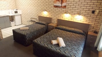 A hotel room with two beds, a kitchenette, and a brick wall.