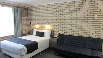 A hotel room with a brick-patterned wall, a bed with a black headboard, a bedside table, and a nightstand.