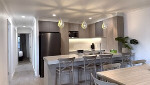 A modern kitchen with a central island, bar stools, a dining table, pendant lighting, and a refrigerator. - Southport Motel & Apartments (Southport)