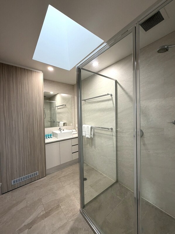 Une salle de bain moderne dotée d’un puits de lumière, d’une cabine de douche en verre et d’un meuble-lavabo avec un miroir.