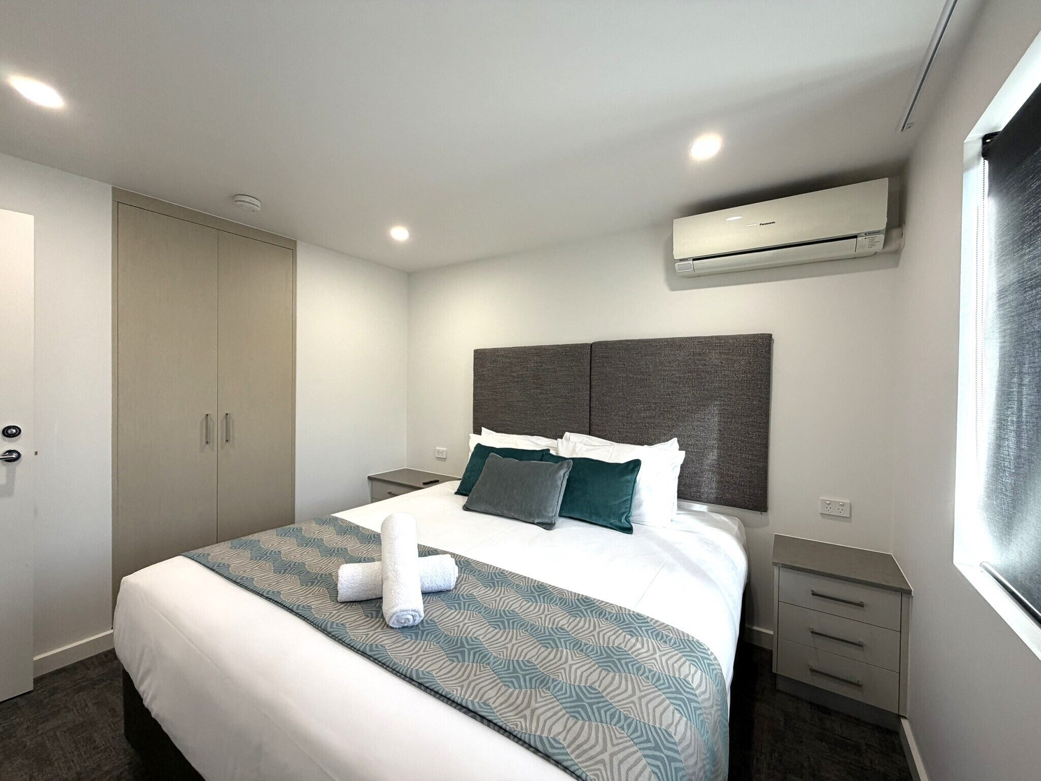 Una habitación de hotel moderna con una cama, mesitas de noche, un armario y un equipo de aire acondicionado.
