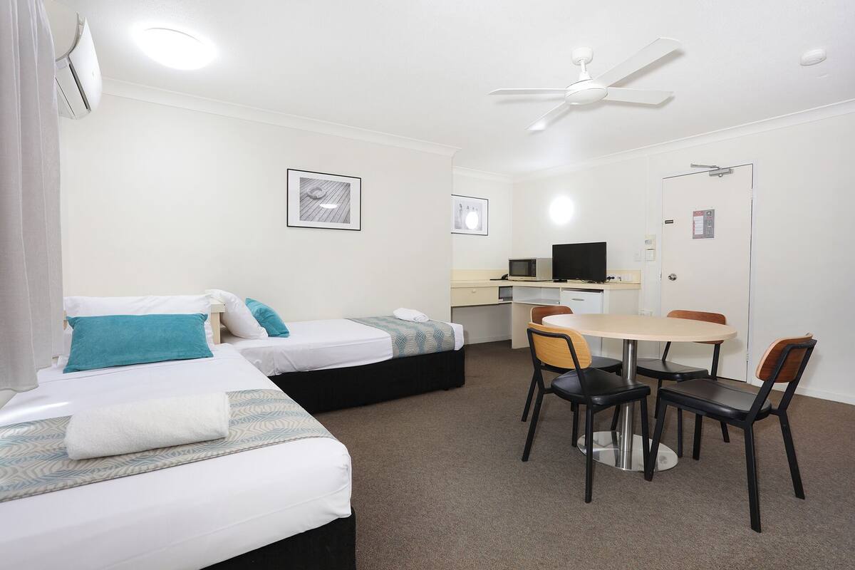 A hotel room with two beds, a desk with a computer, a chair, and a ceiling fan.