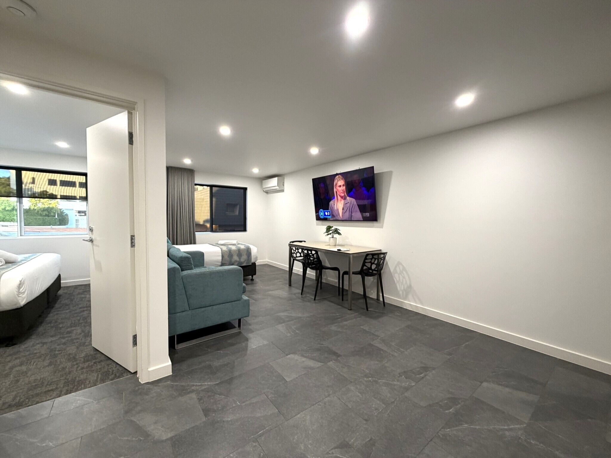 A modern hotel room with a bed, a sofa, a TV, and a dining area.
