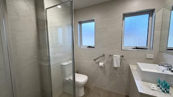 Une salle de bain moderne avec une douche à parois de verre, des toilettes, un lavabo avec un miroir et deux fenêtres.