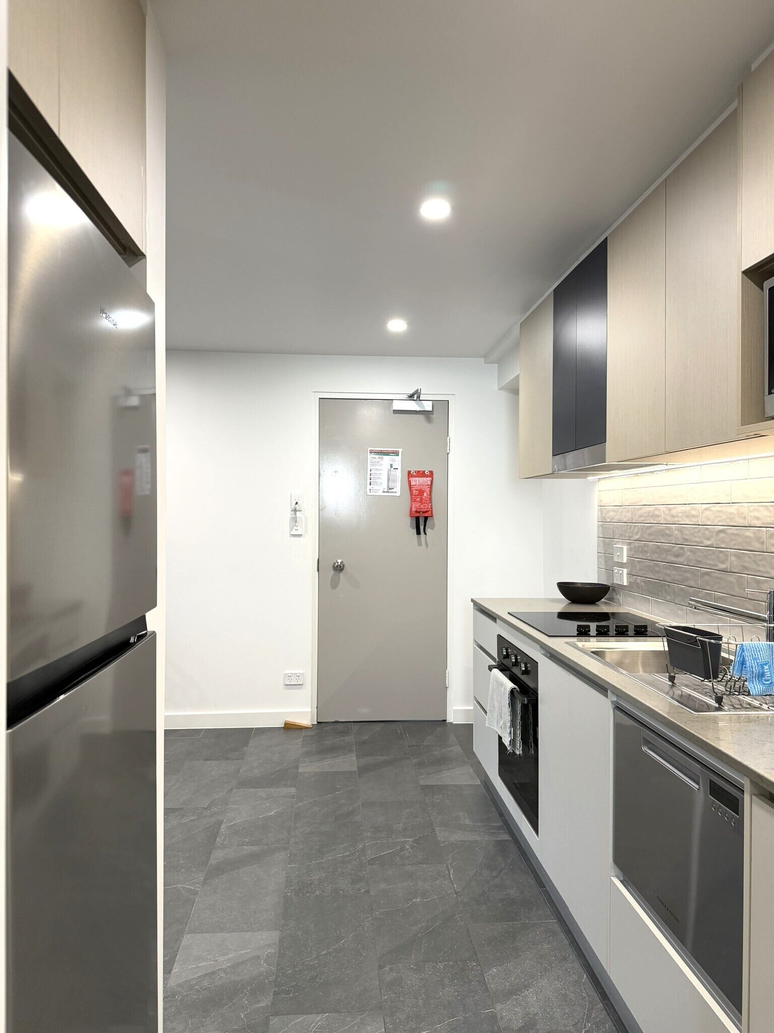 A modern kitchen with stainless steel appliances, grey tiled flooring, and a minimalist design.