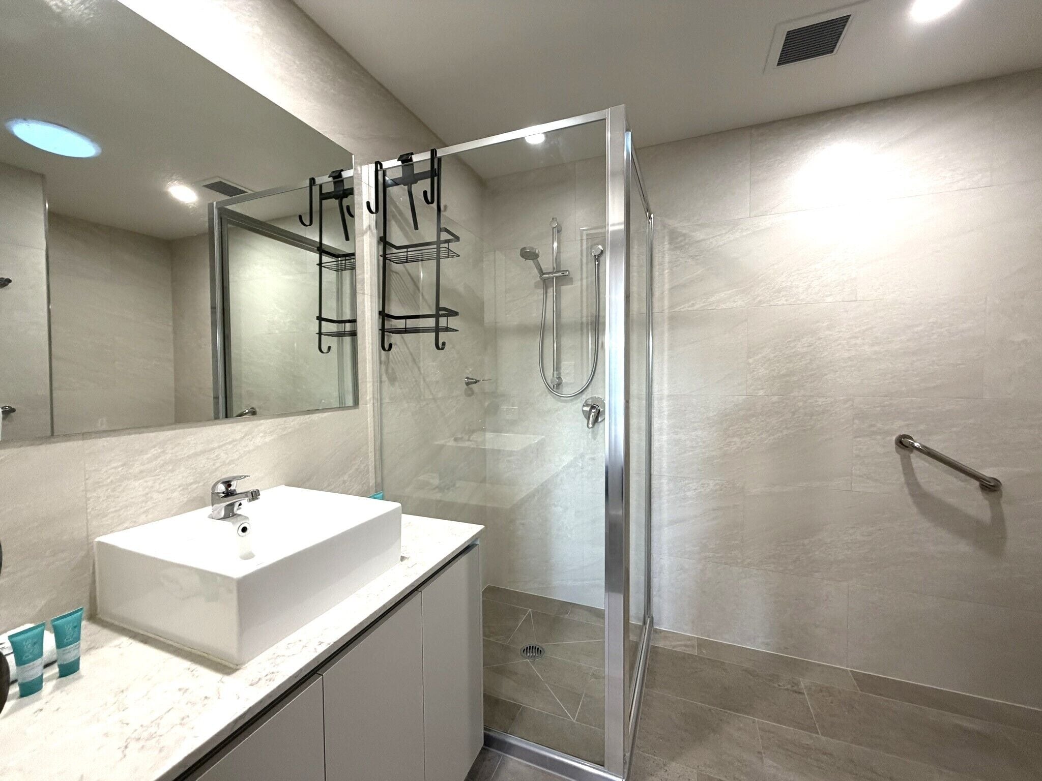 Un baño moderno con ducha de vidrio, lavabo blanco y un espejo grande.