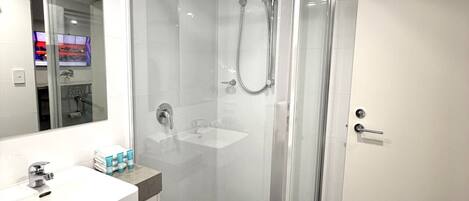 Un baño moderno con ducha envuelta en vidrio, lavamanos con espejo y suelo de baldosas oscuras.