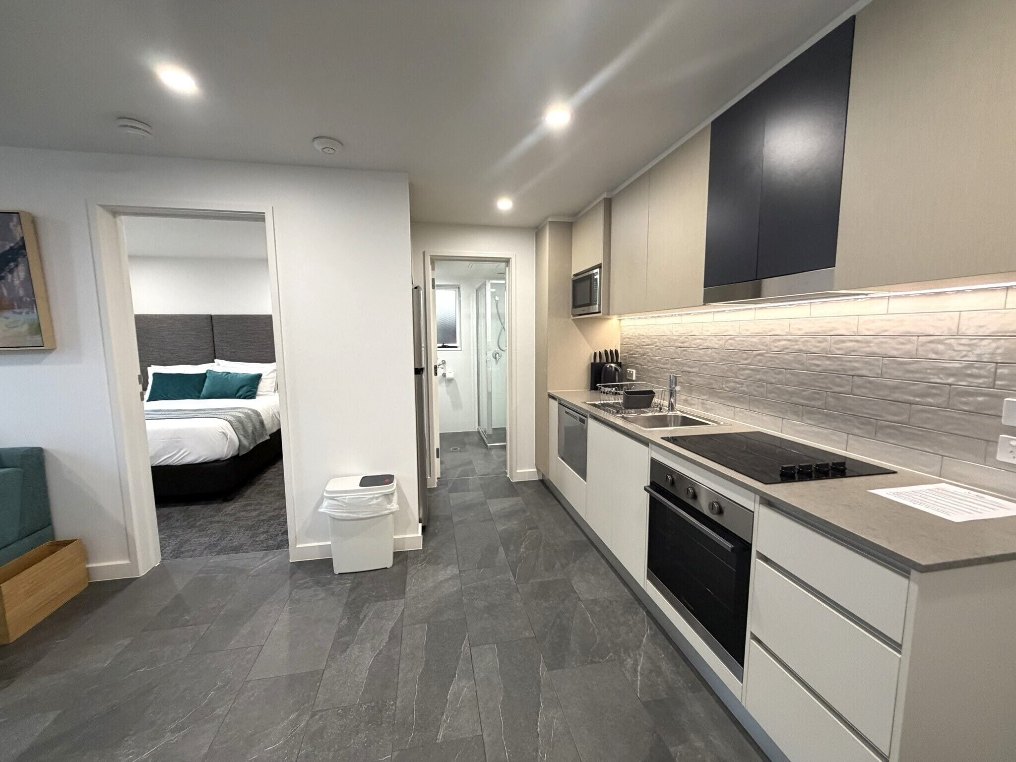 A modern kitchen with a built-in stove, microwave, and sink. There is a separate bedroom visible through an open door.