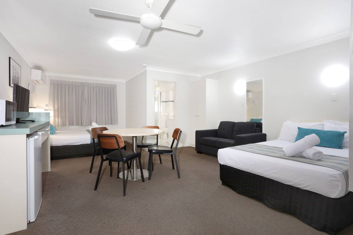 A hotel room with a bed, a desk, a chair, a table, and a ceiling fan.