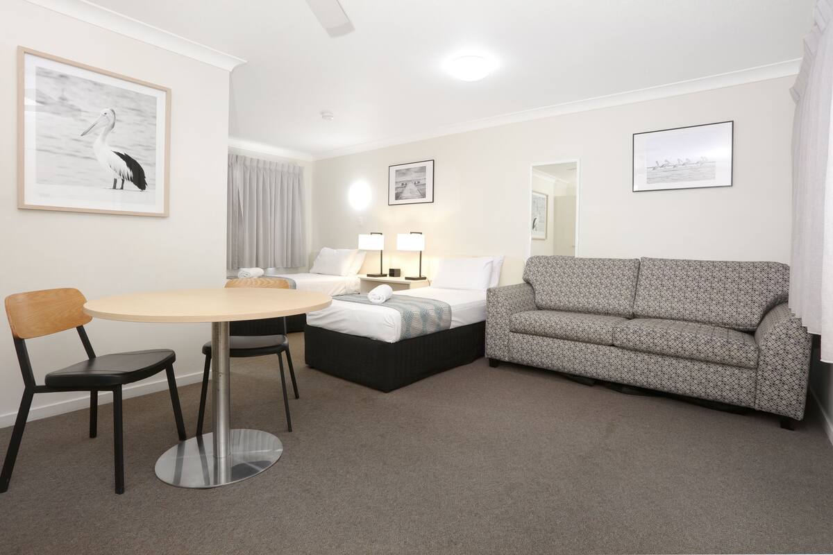 A hotel room with a bed, a sofa, a dining table with chairs, and artwork on the walls.