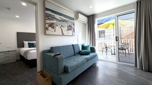 A modern living room with a sofa, a painting, a balcony with chairs, and a view of the outdoors. - Southport Motel & Apartments (Southport)