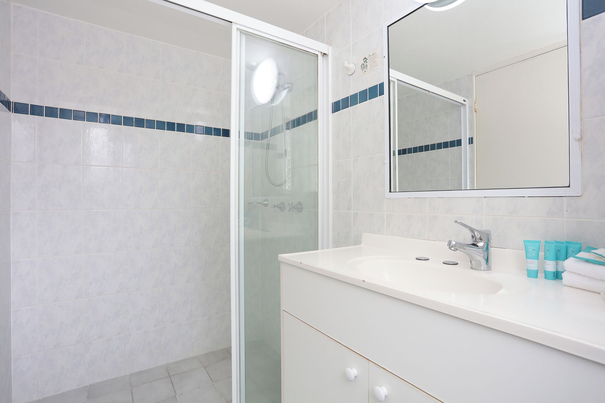 A bathroom with a glass shower enclosure, a white sink with a modern faucet, and a mirror above the sink.