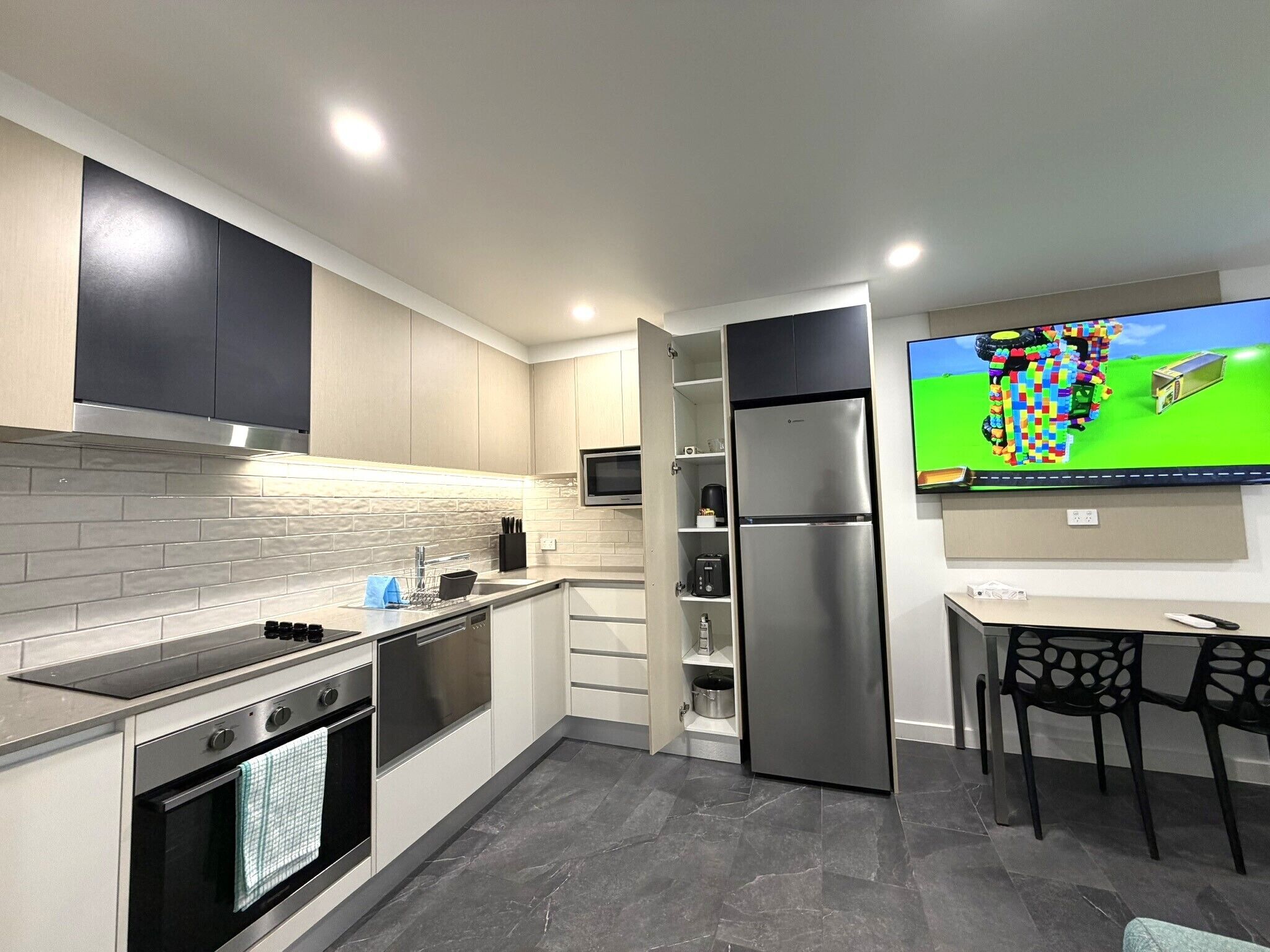 Una cocina moderna con electrodomésticos integrados, una zona de comedor con sillas y un televisor de pantalla plana en la pared.